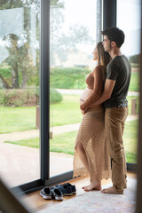 Young man hugging her pregnant woman and looking out the window 