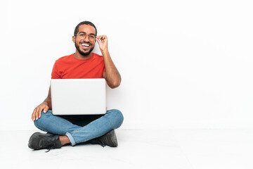 Young Ecuadorian man with a laptop sitting on the floor isolated on white background with glasses and happy