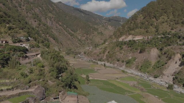 Beautiful farming village farms paddy field vegetables growing in mountainous valley in Kabayan Benguet Philippines wide aerial approaching right trucking revealing valley river mountains blue sky