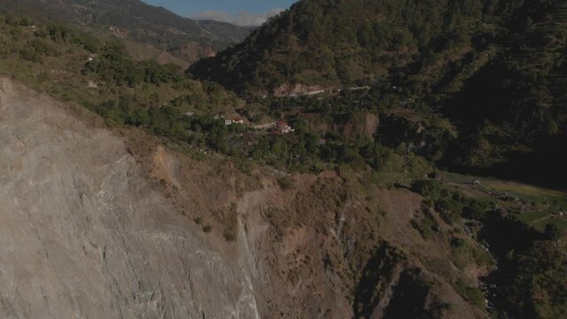 Village on the edge of a cliff in a mountainous region valley surrounded by trees aerial reversing revealing huge rock wall Kabayan Benguet Philippines