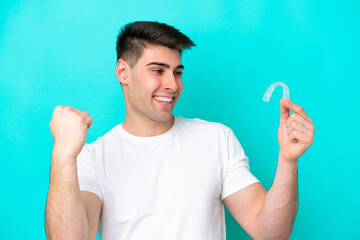 Young caucasian man wearing holding invisible braces isolated on blue background celebrating a victory