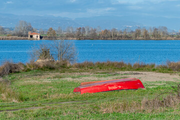 A red wooden boat is capsized near the shore of the Gherardesca lake, Lucca, Italy