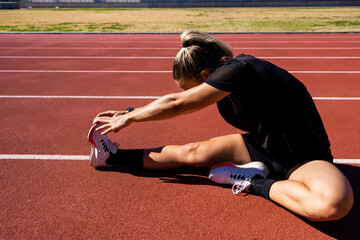 girl sitting on track stretching her leg