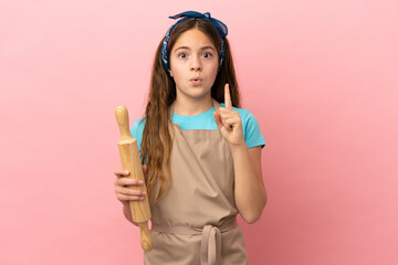 Little caucasian girl holding a rolling pin isolated on pink background intending to realizes the solution while lifting a finger up