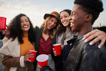 Portrait of diverse group of friends hugging while smiling at camera. Laughing and socializing on rooftop terrace in the evening