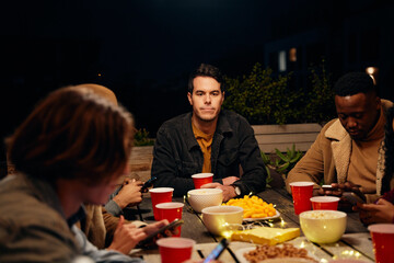 Caucasian male sitting at table at party while all his friends text on their phones. Technology, social media causing anti-social behaviour