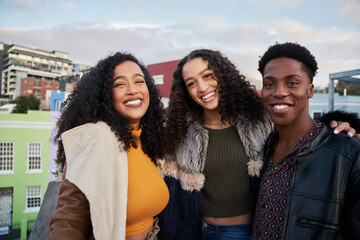 Portrait of diverse group of multi-cultural young adults standing, smiling at camera on a rooftop terrace in city