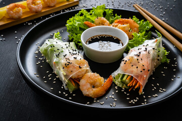 Rice and tapioca paper rolls with prawns and fresh vegetables on wooden black table
