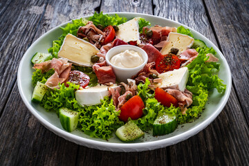 Tasty salad - prosciutto di Parma, camembert and fresh, green vegetables on wooden table
