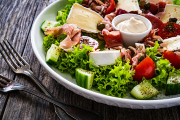 Tasty salad - prosciutto di Parma, camembert and fresh, green vegetables on wooden table
