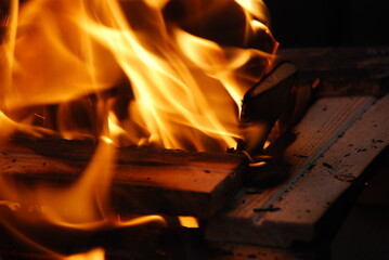 Fire blazes over a fire of wood. A bright yellow-orange flame burns in the dark. Tongues of flame of different lengths and shapes rise above the fire and blaze with heat.