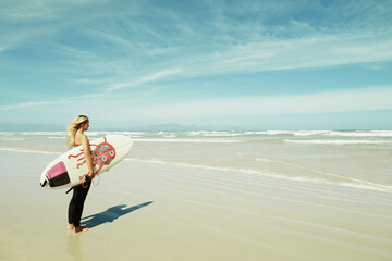Fototapeta na wymiar On her way into the ocean. A young surfer girl holding her surfboard.