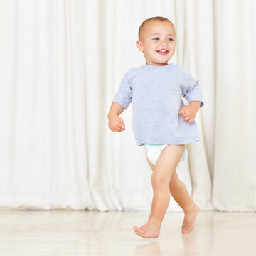 Strutting his stuff. Full length shot of a cute little boy walking around the house in a nappy and t-shirt.