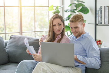 Millennial caucasian lover couple husband and wife in casual outfit sitting smiling on sofa surfing browsing internet shopping online together via laptop notebook computer in living room on weekend