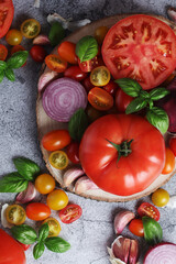 Flat lay composition of different tomatoes, onion, basil and garlic	