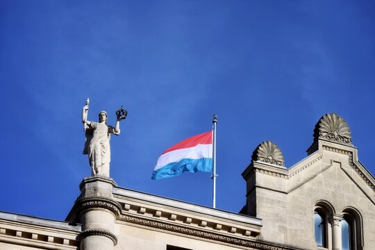 Luxembourg national flag and a figure of an angel on top of Grand Duke palace in Luxembourg, holding sceptre and royal crown