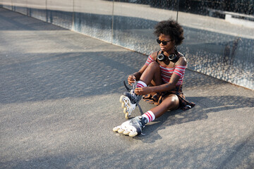 Young woman putting on rollerblades. Beautiful African woman with roller skates