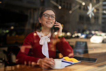 Stylish young woman drinking coffee at cafe. Beautiful girl talking to the phone while enjoy in fresh coffee..