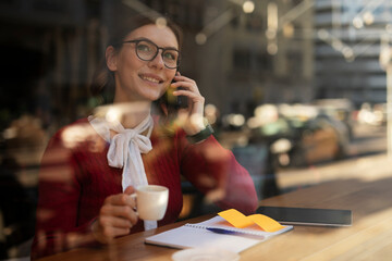 Stylish young woman drinking coffee at cafe. Beautiful girl talking to the phone while enjoy in fresh coffee..
