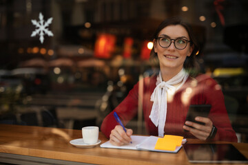Stylish young woman drinking coffee at cafe. Beautiful girl using the phone while enjoy in fresh coffee..