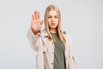 Serious blonde girl showing stop sign and frowning displeased, telling no, refusing something, gray...