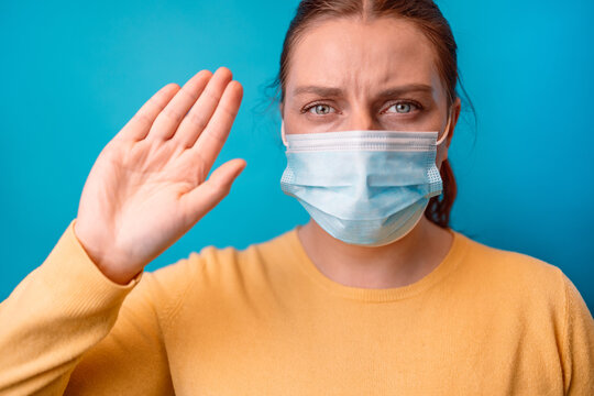 Young woman in a protective medical mask with yellow sweater making stop gesture with her hand with copy space over isolated blue background
