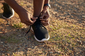 Close up of Black young Adult male athlete tying his shoelaces on his black sports shoe.