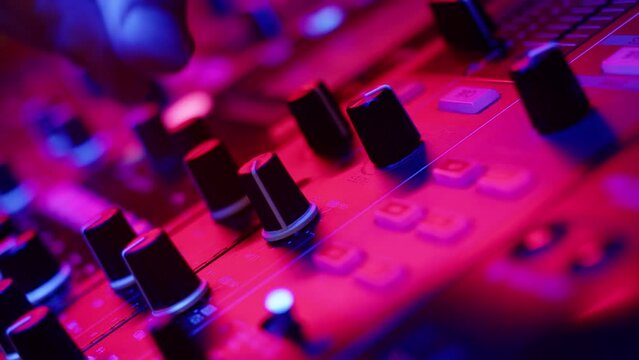 Closeup of DJs hands twisting knobs on mixing console adjusting volume of dubstep in nightclub disco club. DJ sets up hip hop music