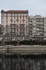 Fototapeta na wymiar View from the river Po of the buildings in the city of Torino. On a cloudy winter day. Some birds flying over the river.