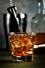 Godfather alcoholic cocktail with scotch whiskey, amaretto liqueur and ice. Dark bar counter background, bar tools, copy space