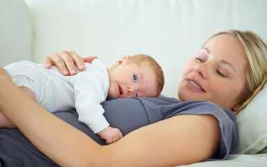 We are too tuckered out. Shot of a mother resting on a sofa with her newborn baby lying on her.
