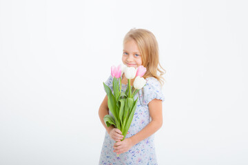 cute little blonde girl in a dress holding a bouquet of spring flowers on a white background. A child holds a bouquet of pink tulips isolated on a white background.