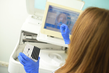 an employee of a medical bacteriological laboratory holds a container with test tubes in his hands against the background of the analyzer.