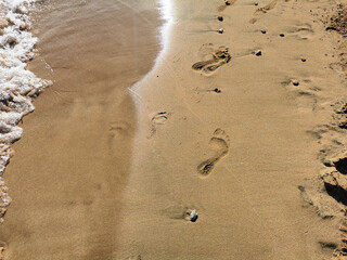 A small wave crashes into the footprints of bare feet on the sand of a beach in Fig Tree Bay.