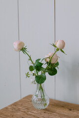 Pink roses in a glass vase on a wooden background