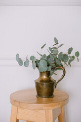 Fresh eucalyptus in a golden vase stands on a chair