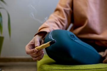Young girl sits in a lotus position and holds Palo Santo in her hands. Scent of incense.