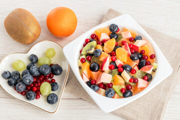Fresh fruit sliced salad in a white bowl of tangerine, grapes, kiwi, apple, blueberries and lingonberries for a healthy diet. 