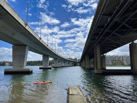 Two people Kayaking through two bridges, Iron Cove Creek pedestrian bridge and Iron Cove Bridge at Bay Run, Sydney NSW Australia