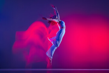 Flight. Young sportive beautiful girl, hip-hop dancer dancing hip hop isolated on purple background in pink neon light. Youth culture, style and fashion, action.