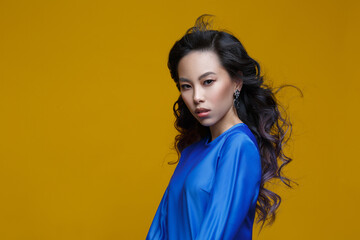 Beautiful Asian girl in a blue dress on a yellow background.