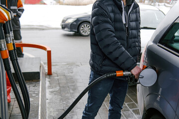 The gray car is refueling at the gas station. The man inserted a gasoline hose into the gas tank.