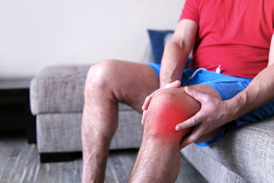 Arthritis is a disease of the joints. A man on a couch, squeezing his knee from excruciating pain.