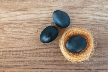 Three blue Easter eggs and a yellow straw nest on a brown background with a wooden texture, flat lay