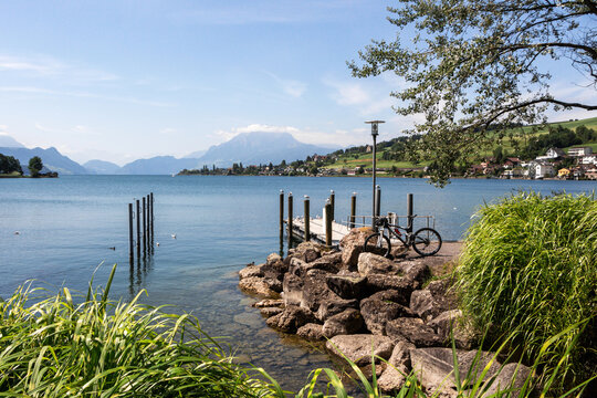 Beautiful landscape of Switzerland with a stone shore and a pier with seagulls on the shore of a transparent lake. Mountain biking as a healthy lifestyle against the backdrop of mountains - Powered by Adobe