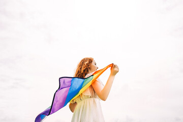 Woman with rainbow flag on sky background.