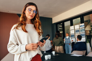 Confident businesswoman holding a smartphone in a boardroom