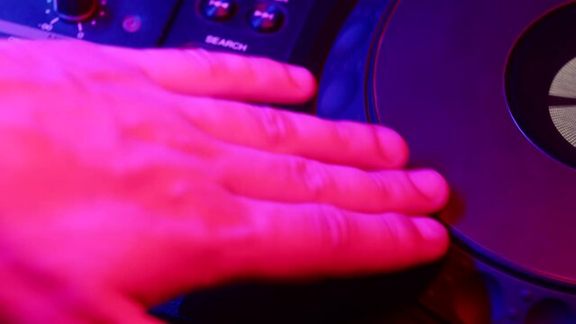 Male DJ's hand presses play button and rotates round platform on digital mixing console, closeup, side view. Concept of professional musical accompaniment at modern parties in nightclub