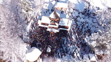 Drone footage of antique wooden church with crowd of people celebrating Christmass in winter Kryvorivnya (Ukraine), covered in snow
