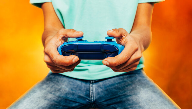 Close up portrait of young boy player hands playing a computer games with pad over fantasy orange background. Online games with friends, youth culture, modern technologies, virtual reality.
